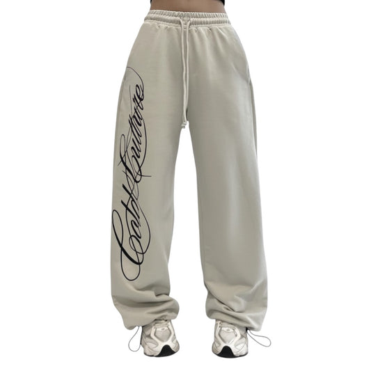 SWAGTOK light beige polyester baggy Y2K sweatpants with black script logo and drawstring waist.