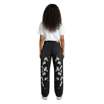 SWAGTOK black denim straight-leg jeans with embroidered white cherry blossoms on the legs. Mid-waist, zip fly.